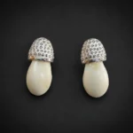 Pareja de pendientes de colmillo de ciervo con casquillo granulado de plata de ley sobre fondo oscuro.