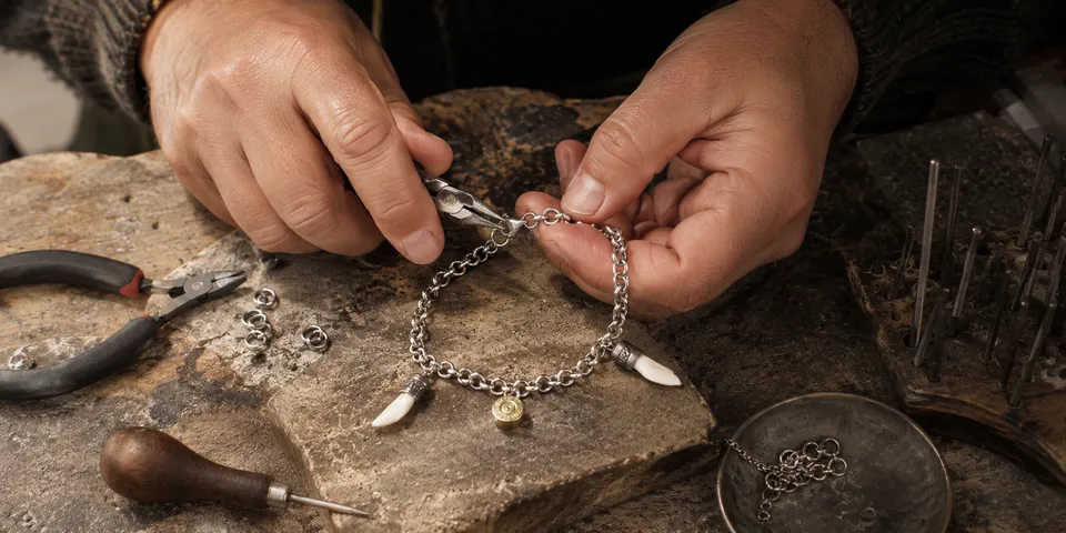 Manos del artesano trabajando una pulsera de acero con dientes naturales de jabalí y colgante de bala