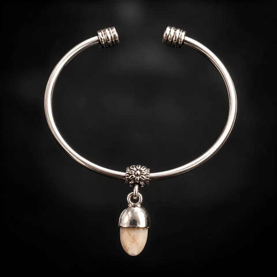 Pulsera rígida de alpaca con colmillo natural de ciervo sobre fondo negro difuminado