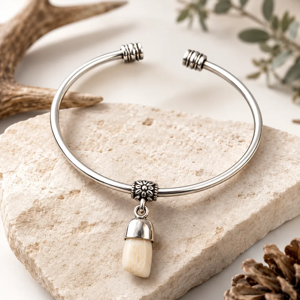 Pulsera rígida de alpaca con colmillo natural de ciervo sobre fondo claro con elementos naturales
