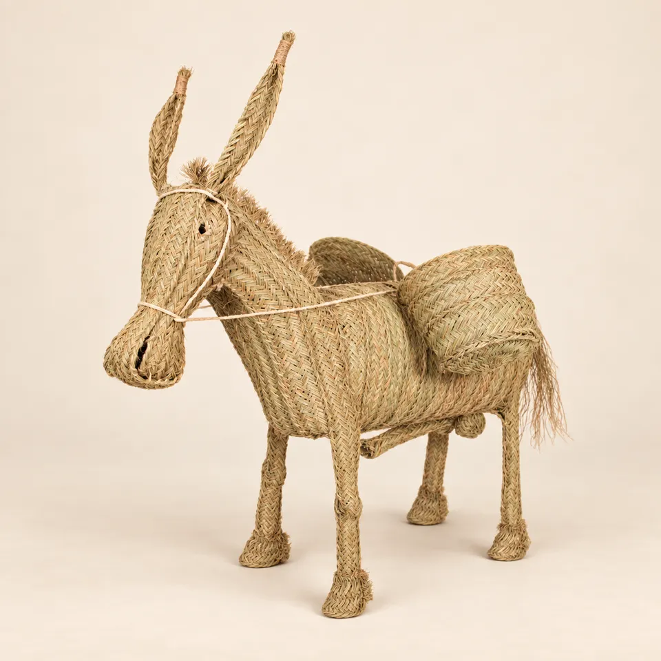 Burro artesanal de esparto con alforjas sobre fondo cálido y claro